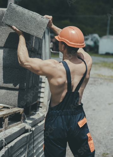 Construction concept. Man carry bricks for construction works. Builder unload truck on construction site. Construction worker in working uniform. Busy working day