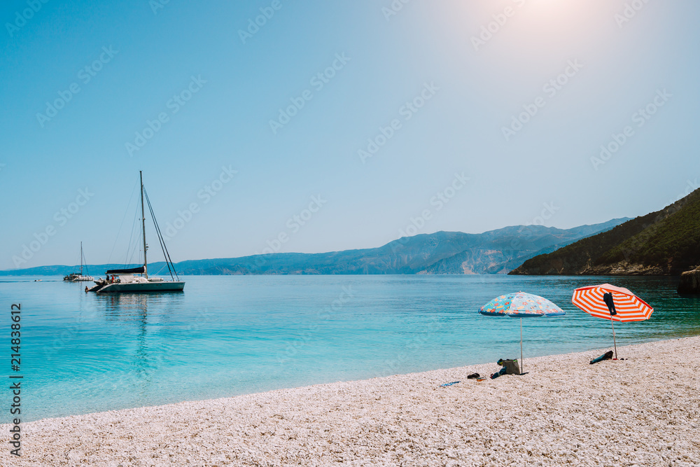 Idyllic white beach with umbrellas on lazy summer day. Sailing boat on calm crystal clear water Idyllic white beach with umbrellas on lazy summer day. Sailing boat on calm crystal clear water