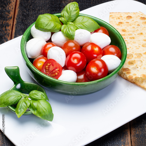 Italian soft cheese, young small balls mozzeralla cheese salad served with fresh basil and tasty ripe cherry tomatoes photo