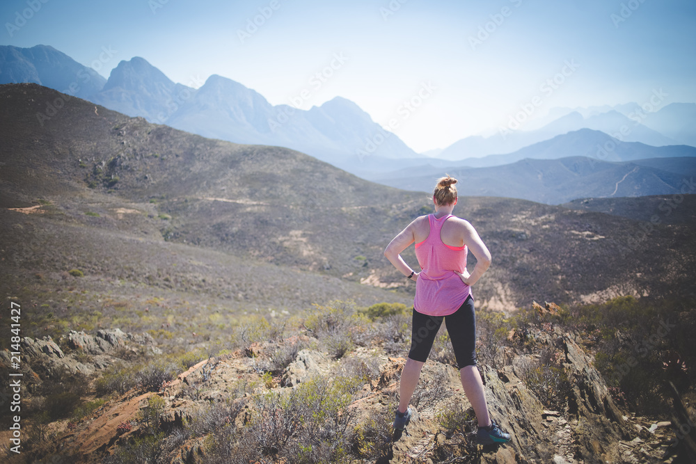 Young blond woman standing on a hill top overlooking the view towards the mountains after doing outdoor exercise