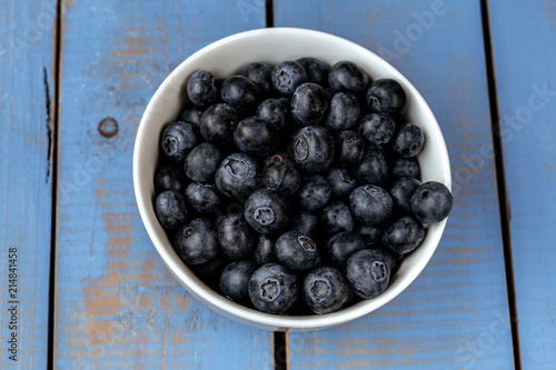 Macro photography of a white bowl full of blueberry on a blue wooden table