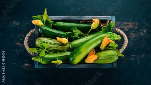 Green zucchini in a wooden box. Fresh vegetables. On a black wooden background. Top view. Copy space.