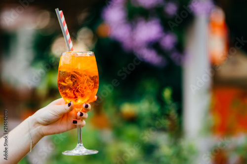 Outdoor shot of fresh cocktail with ice in woman`s hands against blurred background with copy space for your advertising content. Cold beverage for summer party