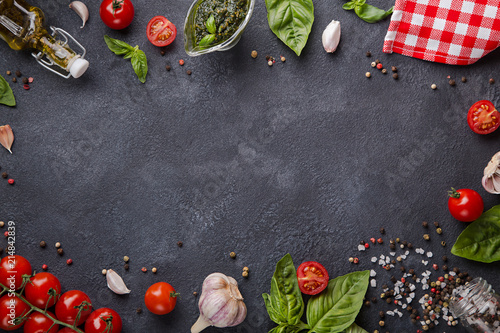 Italian food on dark background with copy space horizontal. Cherry tomatoes, garlic, basil, olive oil, pesto, pepper mix, salt and red napkin