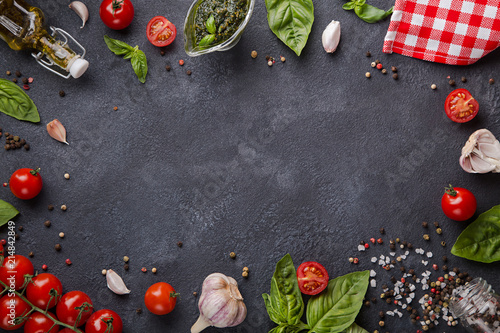 Italian food on dark background with copy space horizontal. Cherry tomatoes, garlic, basil, pesto, pepper mix, salt, olive oil and red napkin