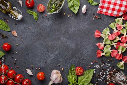 Italian flag farfalle pasta on dark background with copy space horizontal. Cherry tomatoes, garlic, basil, pesto, olive oil, pepper mix, salt and red napkin