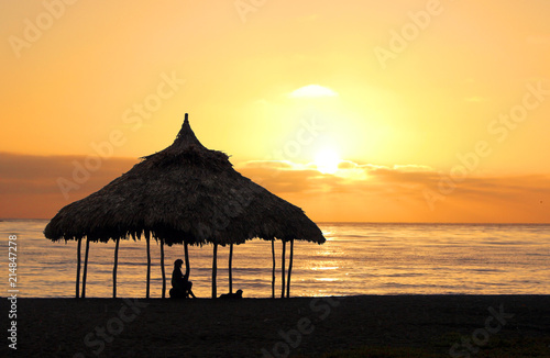 Woman sitting under a cabana on the beach at sunset