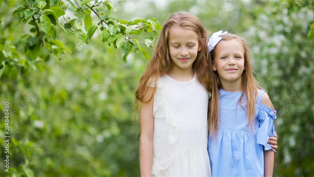 Adorable little girls in blooming apple tree garden on spring day Adorable little girls in blooming apple tree garden on spring day