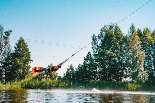 Young man wakeboarding on a lake, making raley, frontroll and jumping the kickers and sliders. Wakeboard. photo