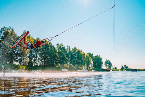 Fotografie Young man wakeboarding on a lake, making raley, frontroll and jumping the kickers and sliders