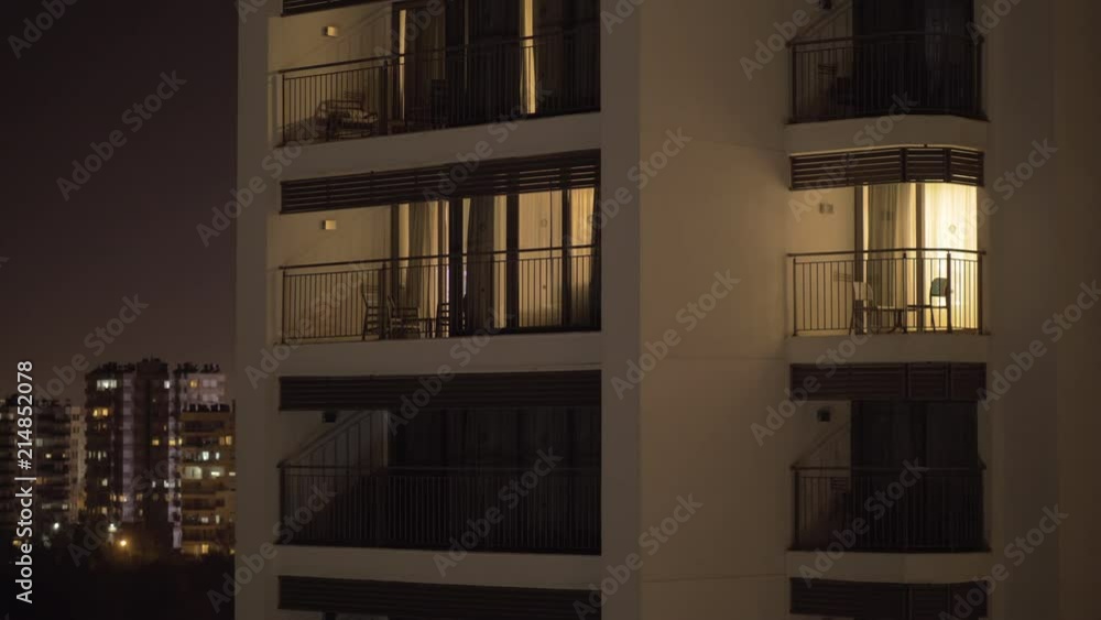 White facade of a multistory hotel looking building. It is night time and the sky is dark so the only visible light is pouring from the hotel windows. On the background there are some similar White facade of a multistory hotel looking building. It is night time and the sky is dark so the only visible light is pouring from the hotel windows. On the background there are some similar
