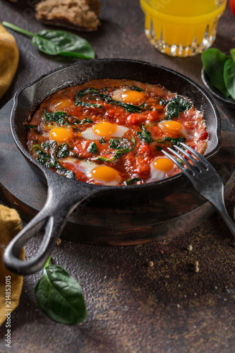 Shakshouka with eggs, tomato, spinach in a pan. Fried eggs in a sauce of tomatoes. Eggs poached with vegetables. Close up