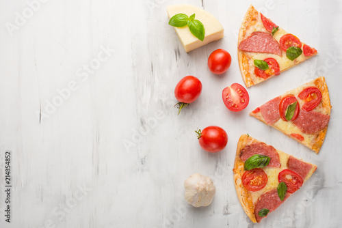 Fototapeta Naklejka Na Ścianę i Meble -  Delicious sliced pizza with tomatoes, mozzarella cheese, basil, and a tomato on a light background,Copyspace. Top view.