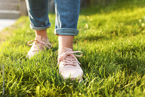Woman in stylish sneakers on green grass, closeup