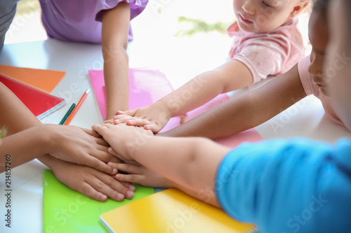 Little children putting their hands together at table, closeup. Unity concept