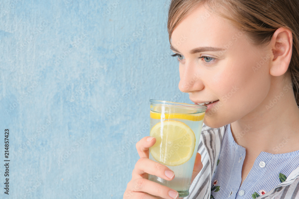 Young woman drinking water with lemon against color background Young woman drinking water with lemon against color background