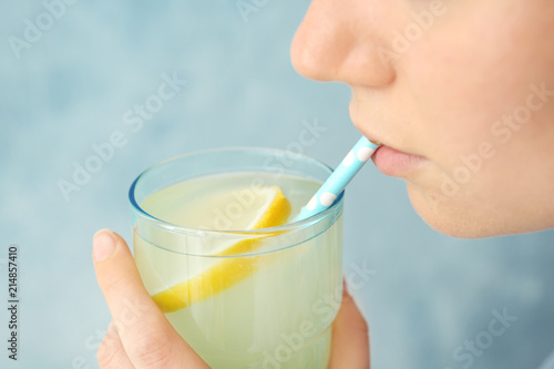 Young woman drinking lemon cocktail against color background