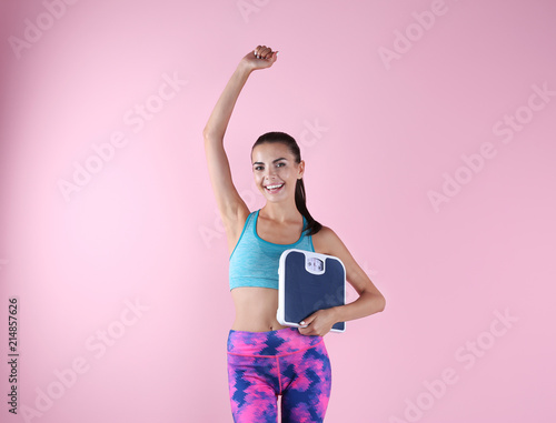 Happy young woman with scales on color background. Weight loss motivation © New Africa