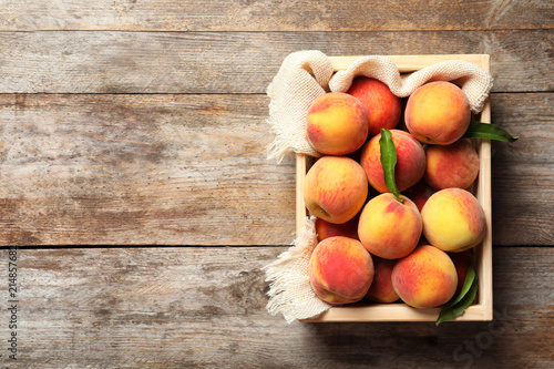 Wooden crate with fresh sweet peaches on table, top view