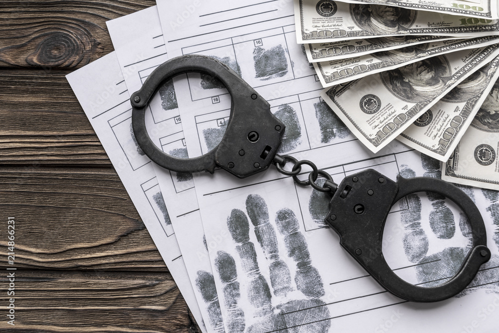 handcuffs, American dollars, fingerprints on the background of a wooden table. detention of the offender. handcuffs, American dollars, fingerprints on the background of a wooden table. detention of the offender.