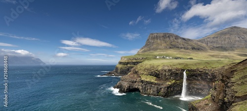 Cliffs with a waterfall near a village, Mykines Island at the rear, Gasadalur, Vagar, Faroe Islands, Denmark, Europe photo