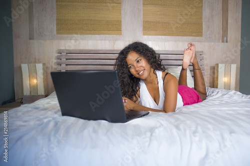 lifestyle portrait of young beautiful and happy black Afro American woman at home bedroom lying cheerful on bed networking using laptop computer