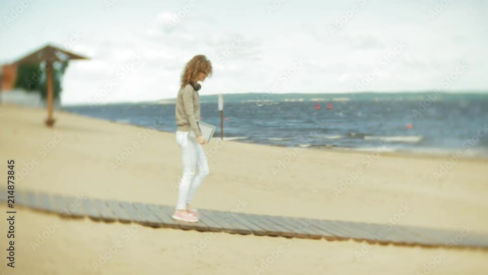 Young beautiful woman is walking the beach in headphones and uses a tablet