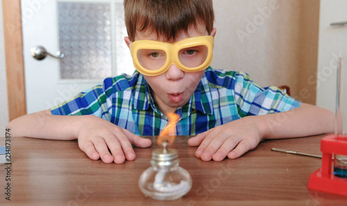 Experiments on chemistry at home. Surprised Boy is looking at the burning alcohol lamp on fire with a match.
