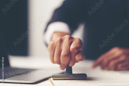 Close-up of a person's hand stamping with approved stamp on certificate document public paper at desk,  notary or business people work from home, isolated for coronavirus COVID-19 protection