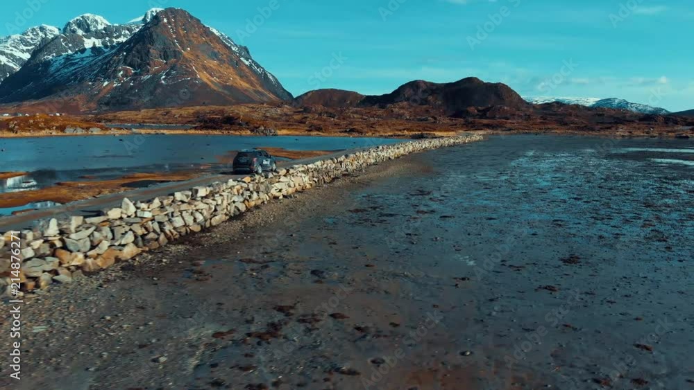 Aerial shot of a car moving on a coastal road with moutains in background Aerial shot of a car moving on a coastal road with moutains in background