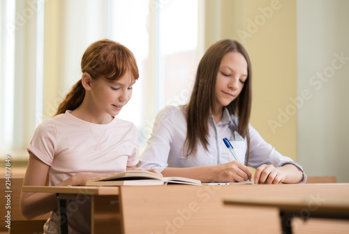 2 student girls are sitting at a Desk