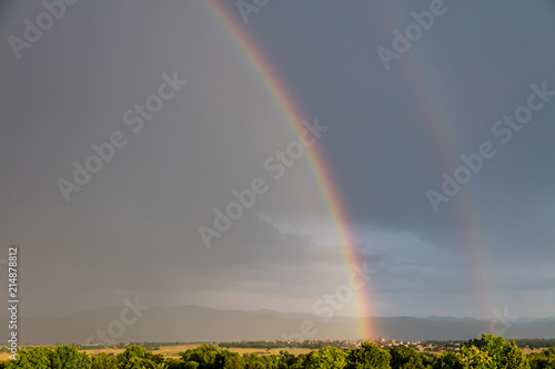 Rainbow over a quaint village and meadows, after the rain, copy space, wallpaper.