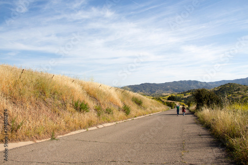 People hiking on a sunny day on a peaceful paved road at Irvine Open Space Hiking Trail in Orange County, Southern California, USA. Healthy outdoor living and exercise.