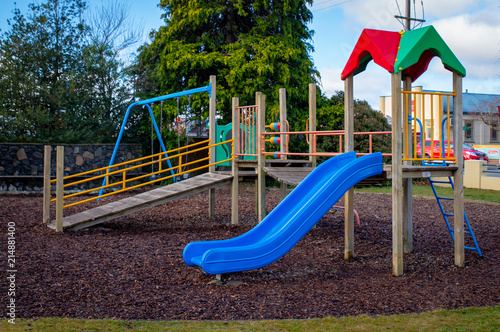 A colourful children's playground with slide and fort and bark chips on the ground