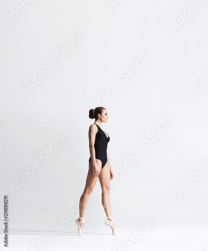 Ballerina in point shoes and bodysuit is dancing in studio. Young and graceful ballet dancer.