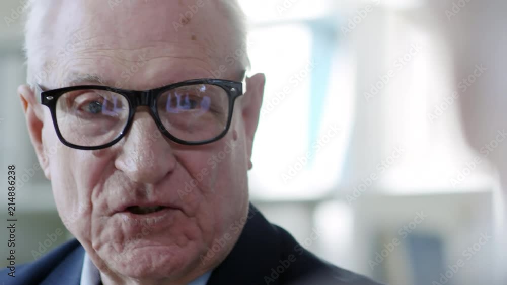 PAN with close up of face of cheerful elderly businessman in glasses and suit talking with unrecognizable colleague on meeting PAN with close up of face of cheerful elderly businessman in glasses and suit talking with unrecognizable colleague on meeting