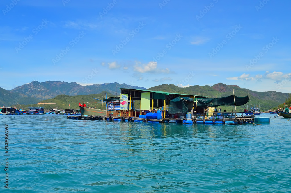 a floating fishing village in a sea bay, against a backdrop of mountains covered with tropical vegetation, clouds and a blue sky, Vietnam