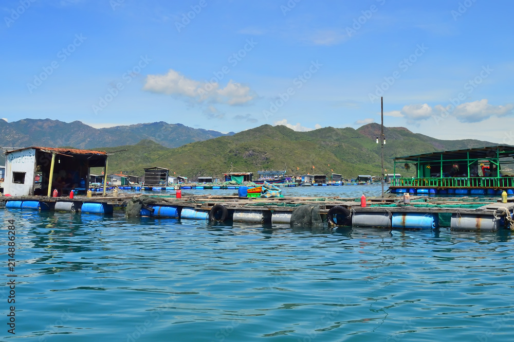 a floating fishing village in a sea bay, against a backdrop of mountains covered with tropical vegetation, clouds and a blue sky, Vietnam