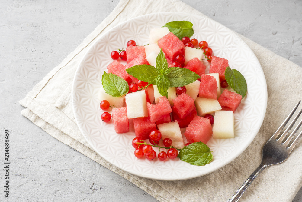 Salad of fresh juicy pieces of watermelon, melon, red currant and mint leaves on a plate. Salad of fresh juicy pieces of watermelon, melon, red currant and mint leaves on a plate.