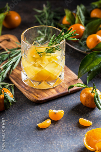 Alcoholic cocktail with tangerines, juice, rosemary and ice on a dark background, copy space