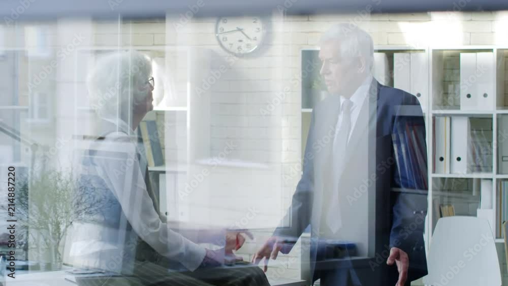 PAN shot through glass: senior female executive with grey hair sitting on her desk and chastising disgruntled elderly businessman in suit PAN shot through glass: senior female executive with grey hair sitting on her desk and chastising disgruntled elderly businessman in suit