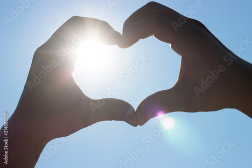 heart shaped made of hands against the sky, sunlight flare