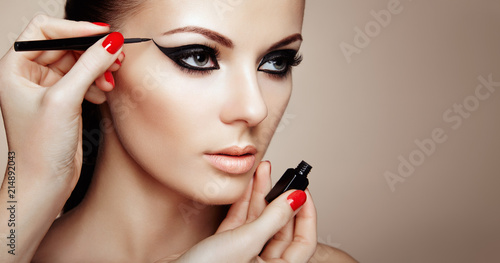 Makeup Artist Applies Eyeshadow. Beautiful Woman Make-up Eye with Black Liner. Fashion Makeup Arrows. Red Nails Perfect Skin photo