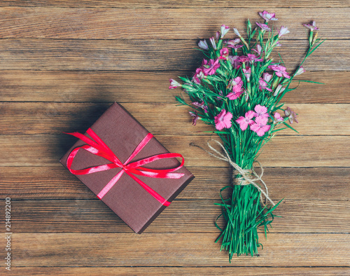 Fototapeta Naklejka Na Ścianę i Meble -  bouquet of carnations and brown box with a gift on a wooden background, flat lay top view