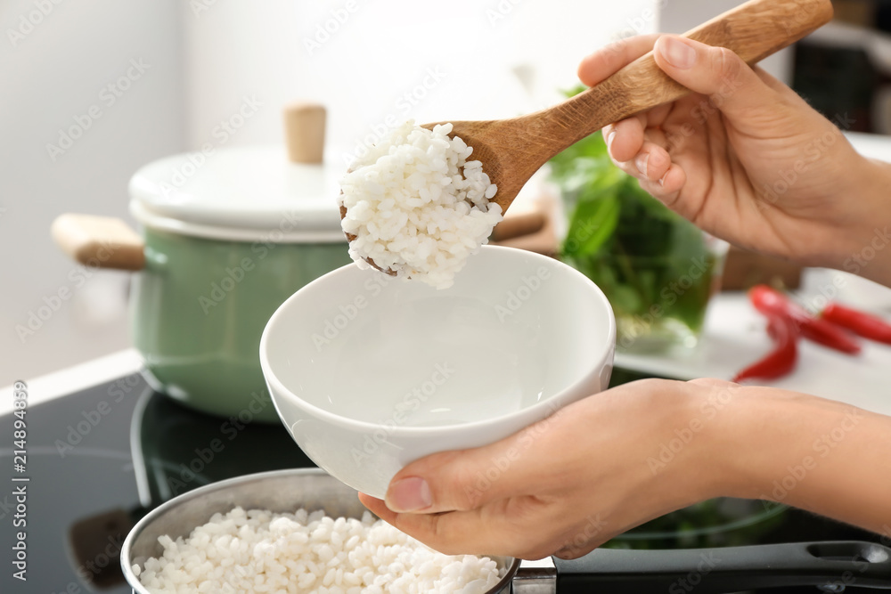 Woman putting boiled rice into bowl in kitchen, closeup Woman putting boiled rice into bowl in kitchen, closeup