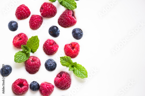 Fresh raspberries and blueberies with mint on yogurt background