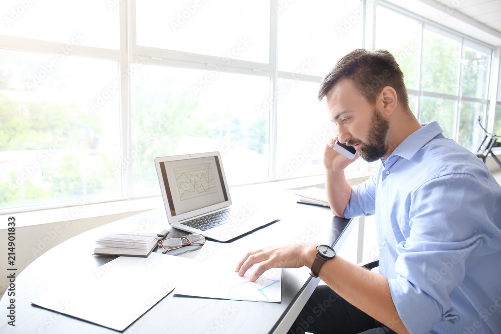 Businessman talking by phone while working in office Businessman talking by phone while working in office