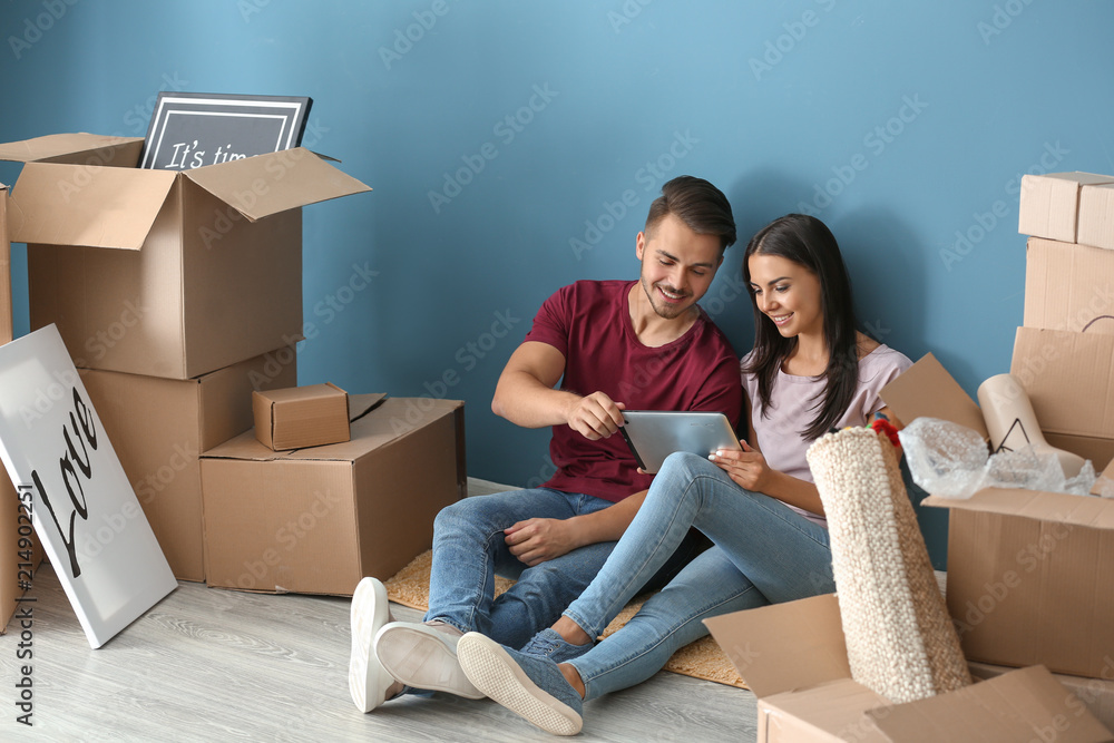 Young happy couple with tablet PC and moving boxes sitting on floor at new home Young happy couple with tablet PC and moving boxes sitting on floor at new home