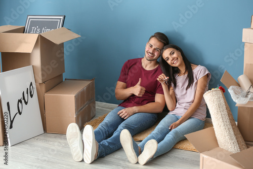 Young happy couple with key and moving boxes sitting on floor at new home © Pixel-Shot