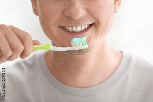 Man brushing his teeth on light background, closeup